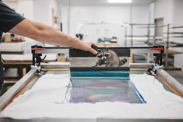 Proses afdruk sablon kaos menggunakan screen, emulsi, dan film desain untuk hasil cetak tajam dan presisi